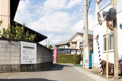 「駐車場〜店舗】駐車場から国道を南へ向かって歩いていくと右手の細い道からピンクのノボリが見えます。店舗前にも駐車は可能ですが運転に不安がある方は大型駐車場へお止め下さい。店舗ブロック塀に設置した白い看板が目印です。 - クリエイト☆ラボの外観の写真