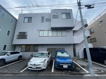 ・駐車場の奥の3階建ての灰色のビルの1階 - STUDIOFLAG北千住2号店の室内の写真